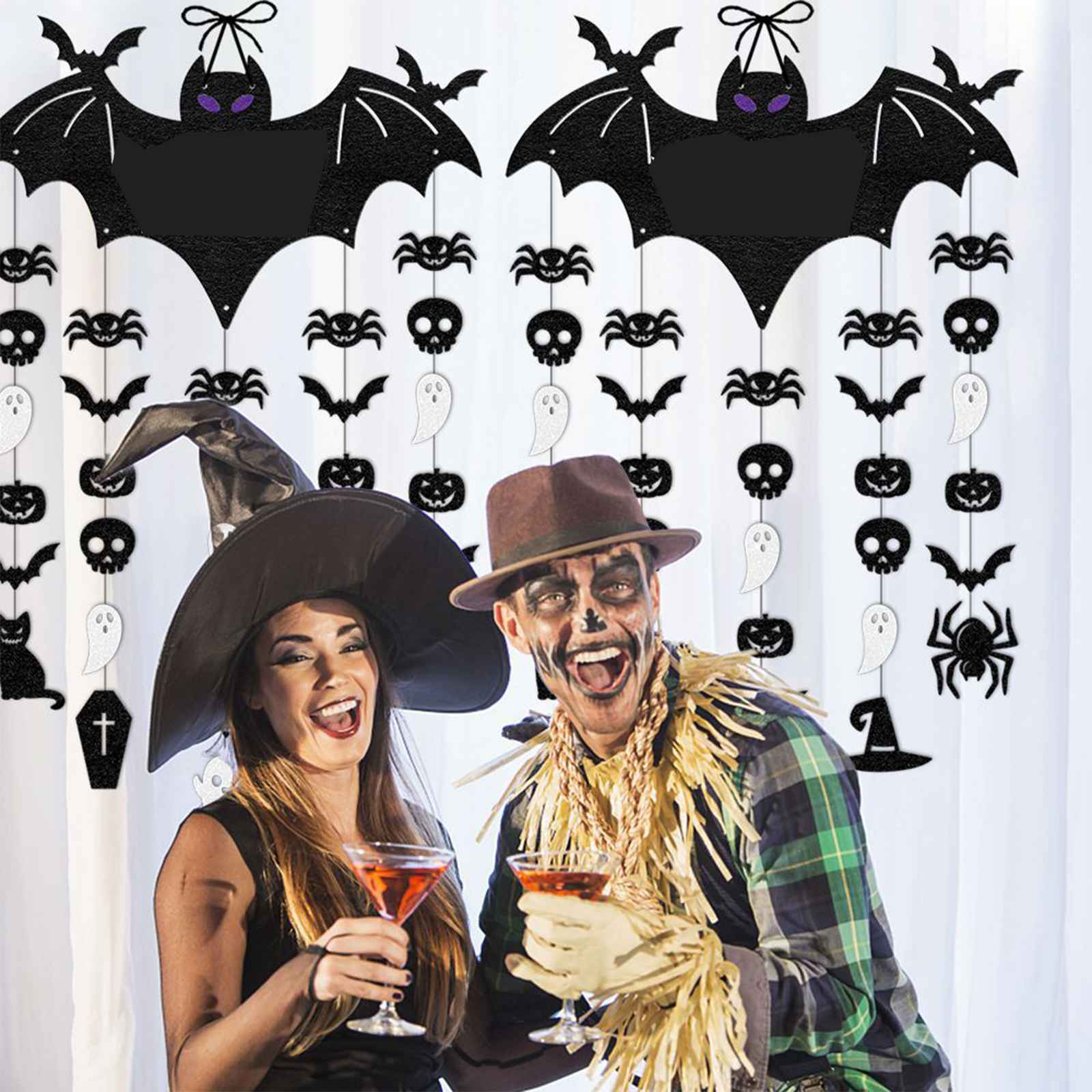 Ein Paar in Halloween-Kostümen hält Cocktails. Dekorationen mit Fledermäusen, Spinnen und Totenköpfen sind im Hintergrund.
