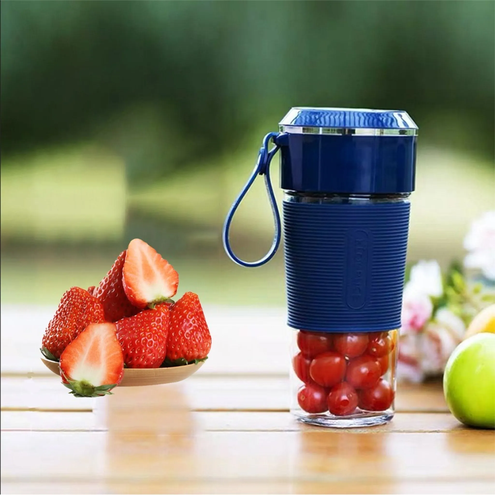 Ein blauer Mixer mit Tomaten und ein Teller mit Erdbeeren. Grüner Hintergrund und Holztisch.
