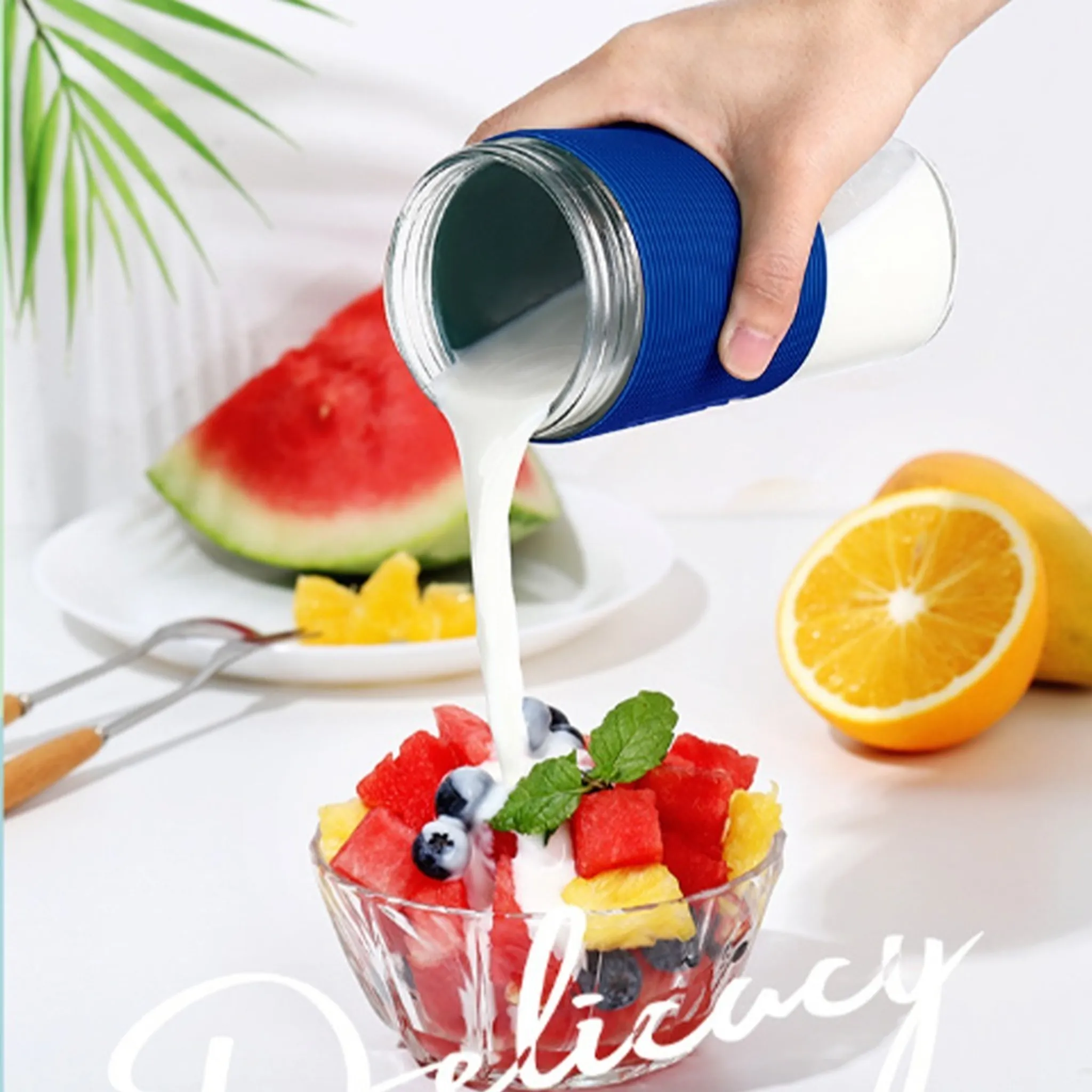 Eine Hand gießt Milch aus einem Glas in einen Obstsalat. Wassermelone, Orangenscheiben und Blaubeeren sind in der Schüssel.