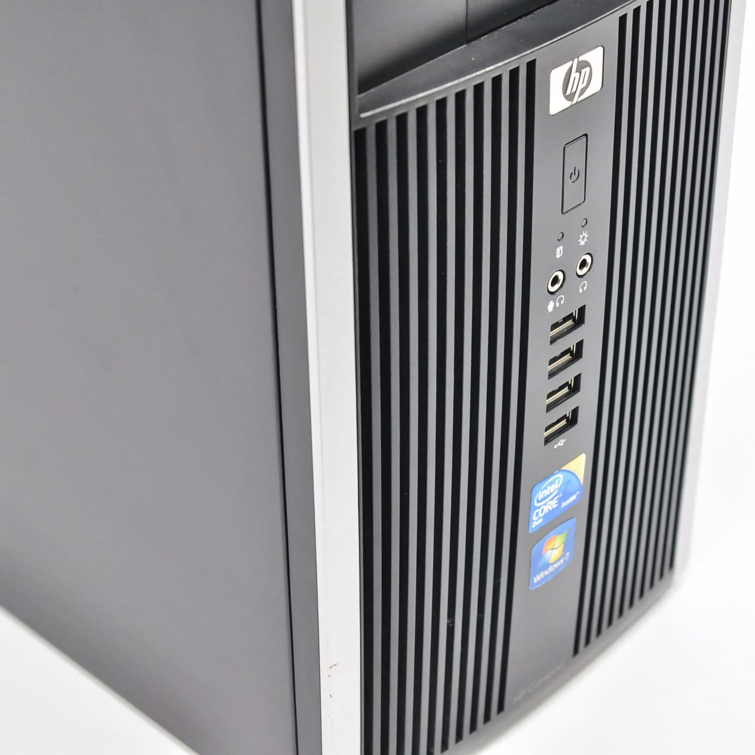 Una torre de computadora HP. El panel frontal tiene líneas verticales y el logotipo de HP. Se ven puertos de alimentación y USB.