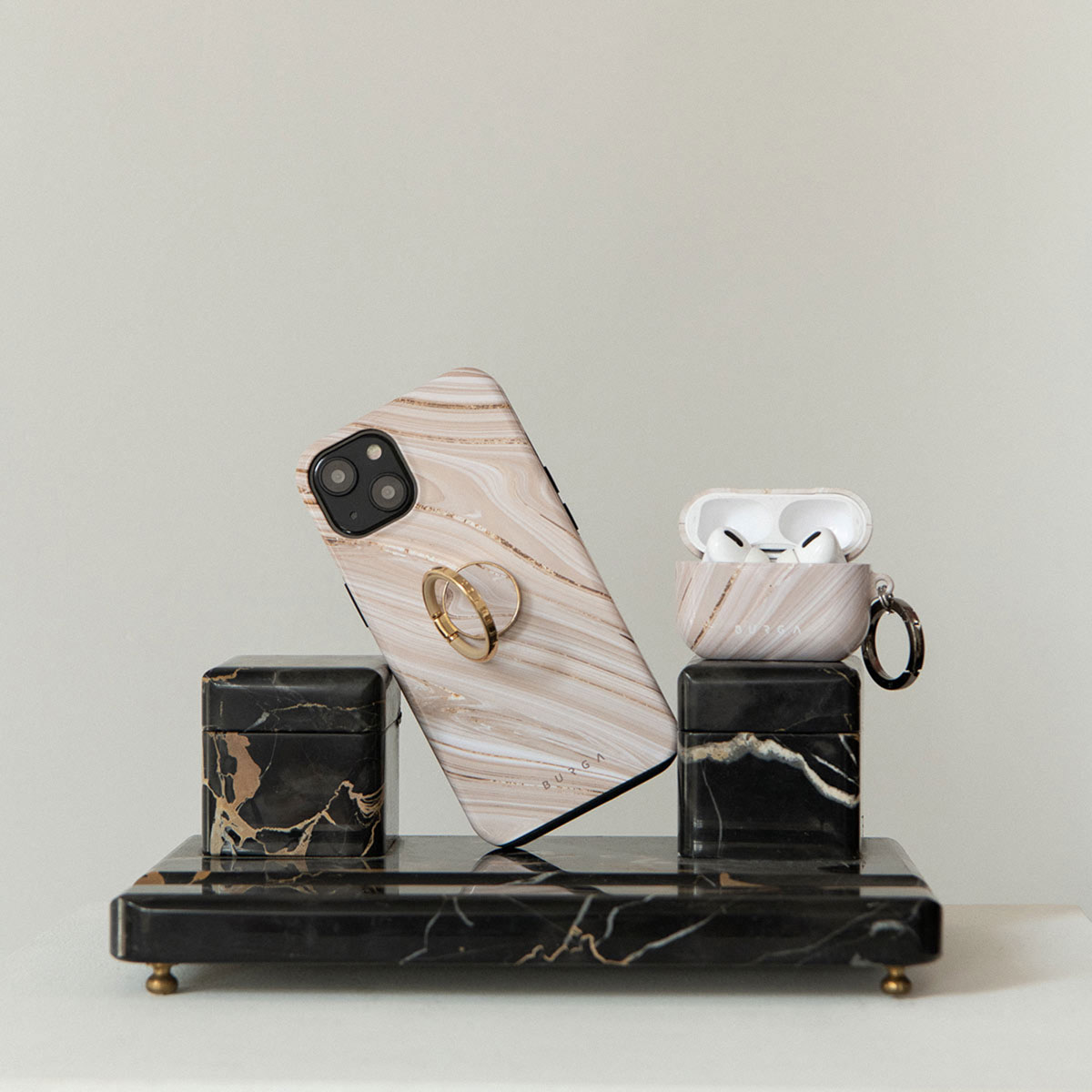 Een telefoonhoesje en AirPod-hoesje met marmerdesign, rustend op een zwart marmeren standaard met gouden accenten en een witte achtergrond.