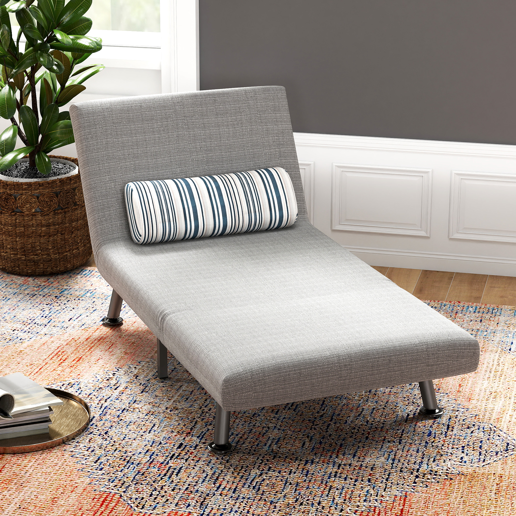 Una chaise longue grigia con cuscino a righe, tappeto multicolore e pianta in vaso.