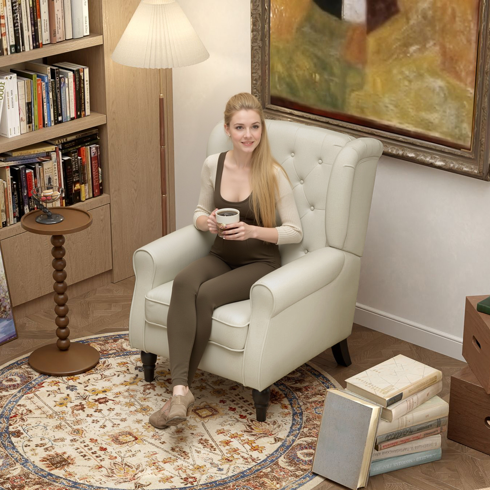 Donna con lunghi capelli biondi seduta su una sedia bianca, tiene una tazza. Librerie e una lampada sullo sfondo.