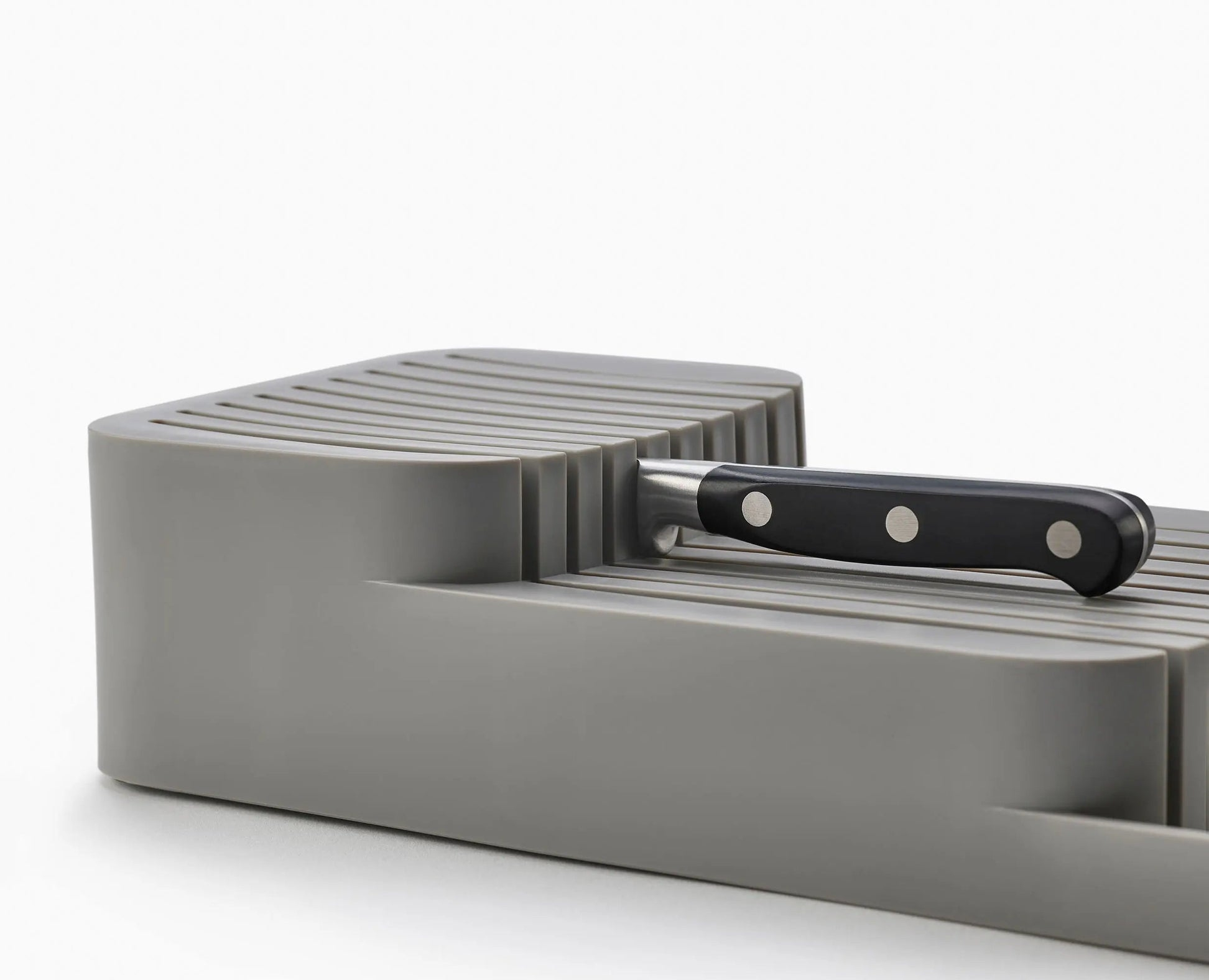 Un bloque de cuchillos gris con un cuchillo de mango negro insertado. El fondo es blanco.
