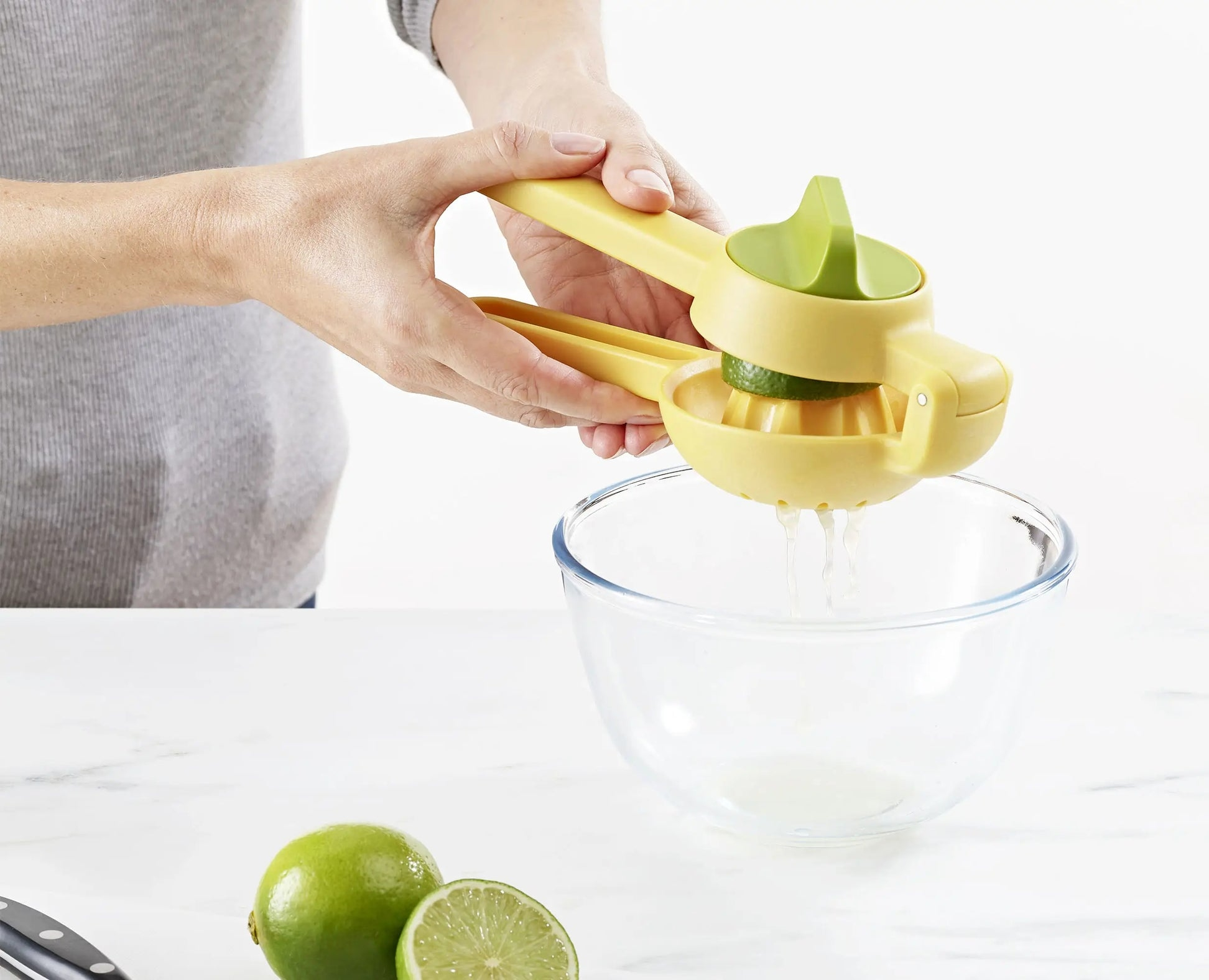 Una persona che spremi una lime con uno spremiagrumi giallo in una ciotola di vetro, con lime sul tavolo.