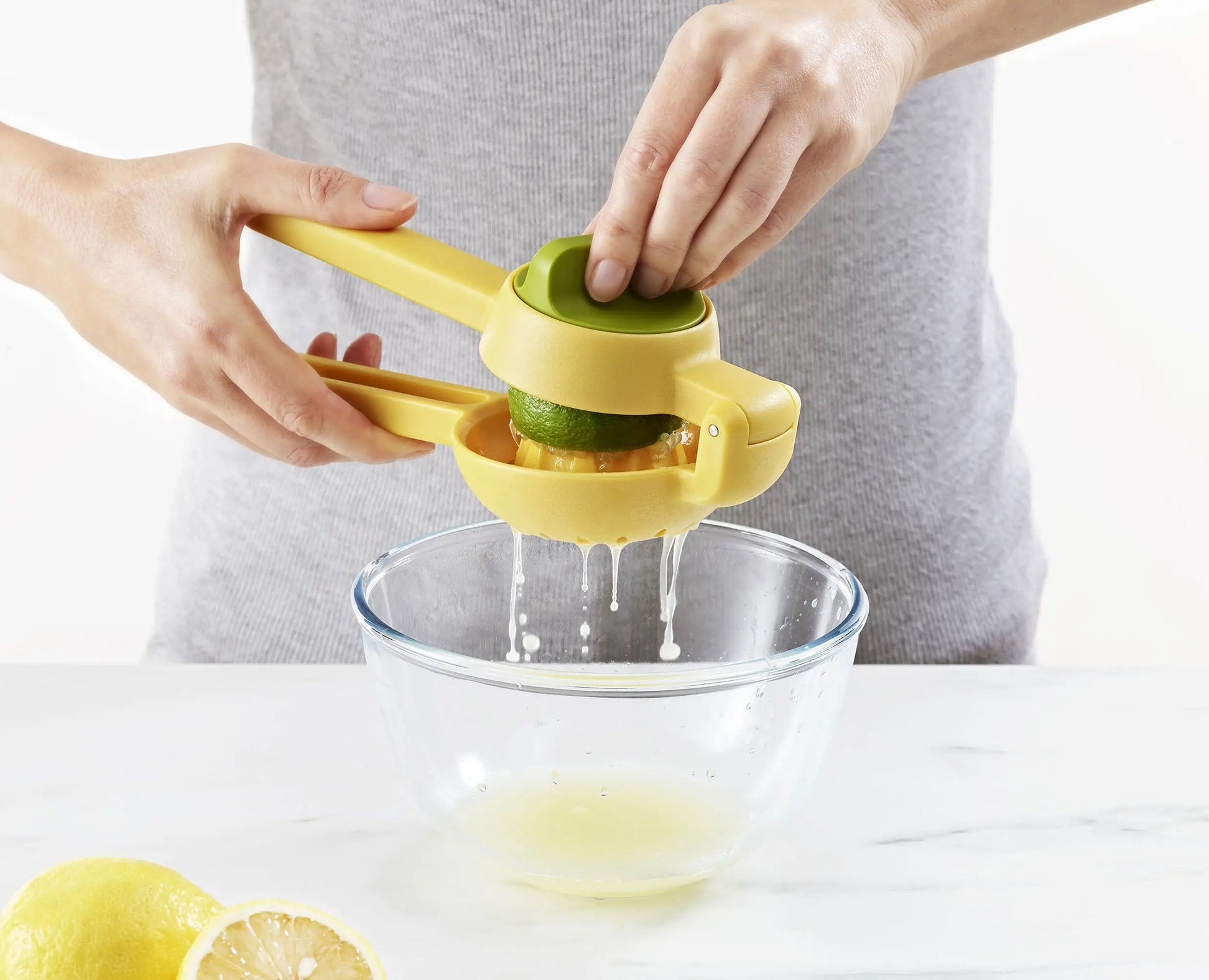 Una persona sta spremendo un lime con uno spremiagrumi giallo sopra una ciotola di vetro. Limone e mezzo limone in primo piano.