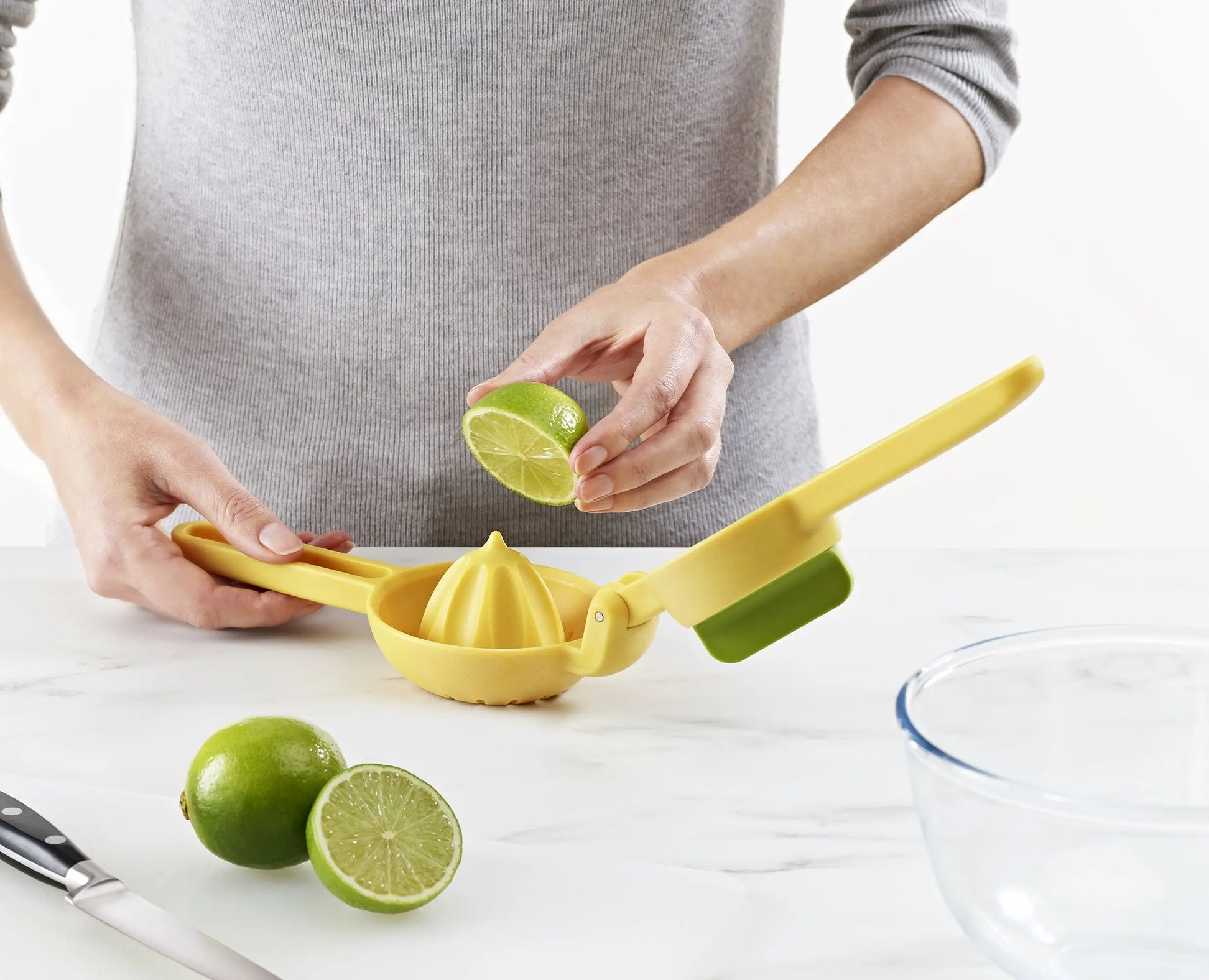 Una persona sta spremendo un lime con uno spremiagrumi giallo. Ci sono lime, un coltello e una ciotola sul tavolo.