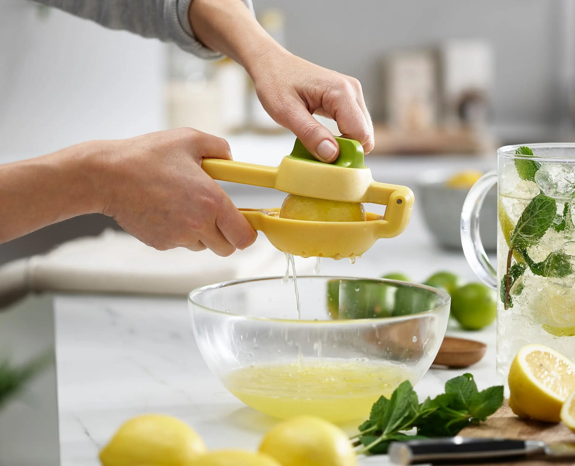 Una persona che spremi il succo di limone con uno spremiagrumi giallo in una ciotola. Si vedono anche menta e limoni.