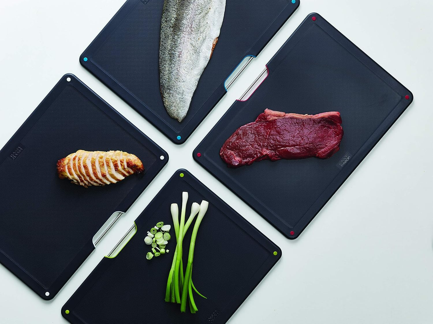 Cuatro tablas de cortar negras con comida: pescado, bistec, pollo y cebolletas. Las tablas tienen puntos de esquina de colores.