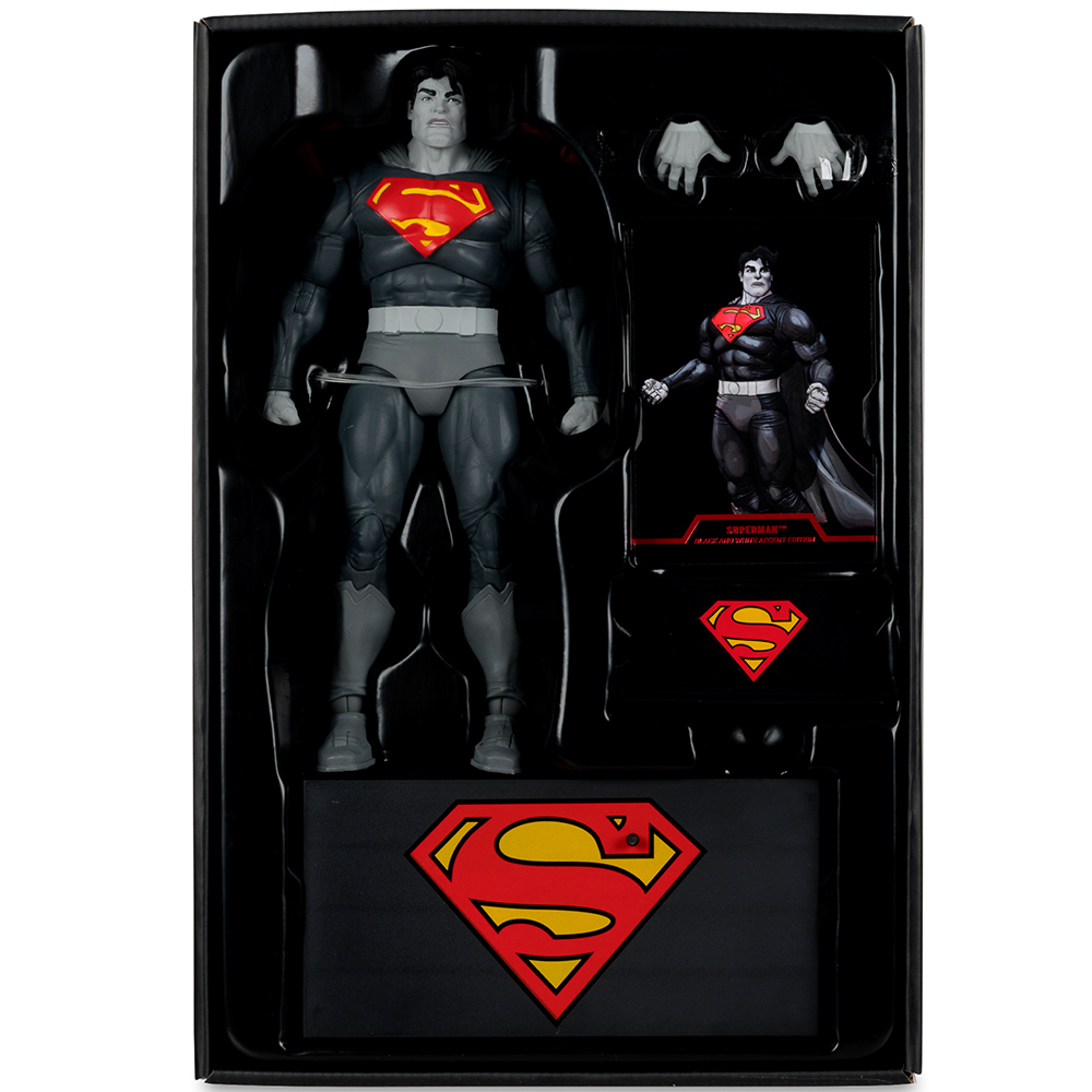 Action figure di Superman in una scatola nera. La figura è grigia con una S rossa e gialla sul petto. Include mani e una mini figura.