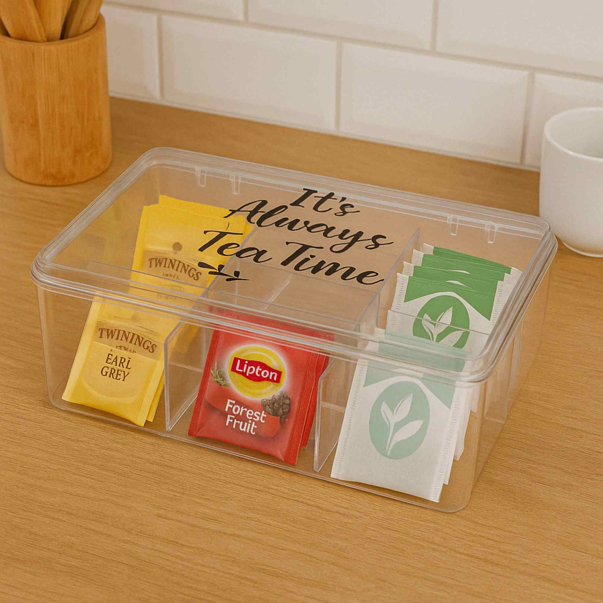 Una caja de té transparente con bolsitas de té: Twinings Earl Grey, Lipton Forest Fruit y té verde. Dice 'It's Always Tea Time'.