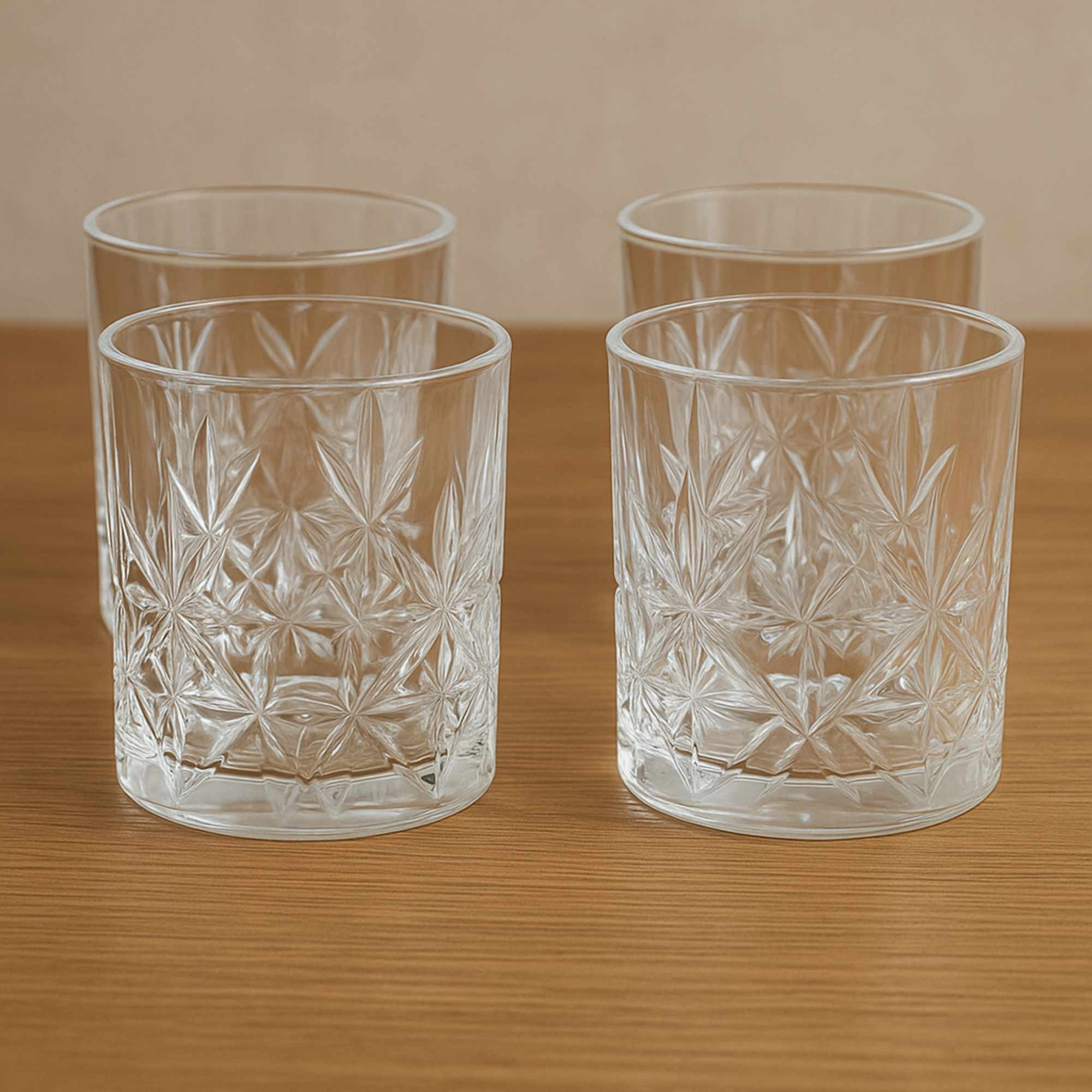Cuatro vasos transparentes estampados sobre una mesa de madera. El fondo es una pared beige.
