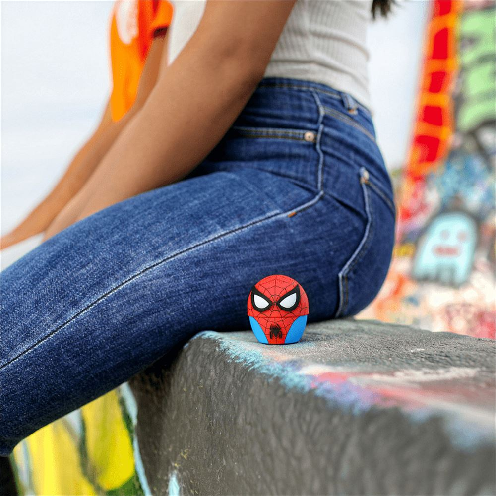 Una persona seduta con jeans blu, un altoparlante di Spider-Man di fronte. Lo sfondo ha arte di graffiti. L'altoparlante è rosso, blu e bianco.