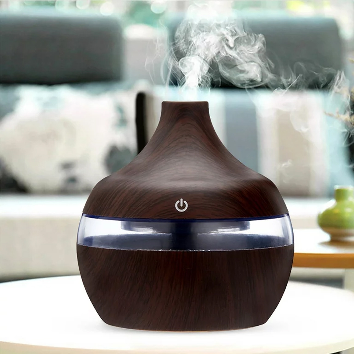 Ein dunkler Holzluftbefeuchter mit Ein-/Ausschalter, der Dampf abgibt. Auf einem weißen Tisch platziert. Hintergrund: Sofa und Vase.