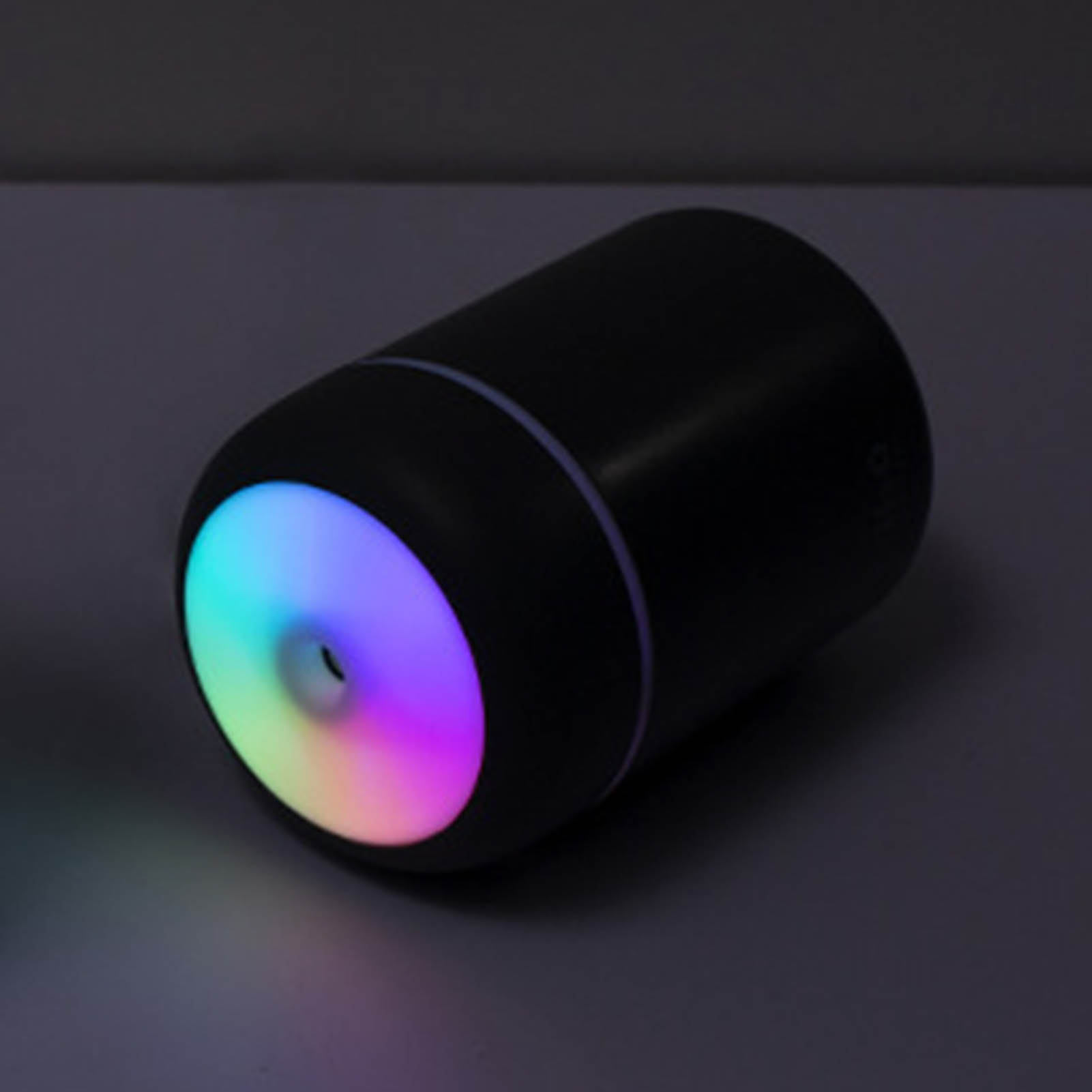 Ein schwarzer Luftbefeuchter mit farbigem Licht. Das Licht scheint in Regenbogenfarben, auf dunklem Hintergrund.