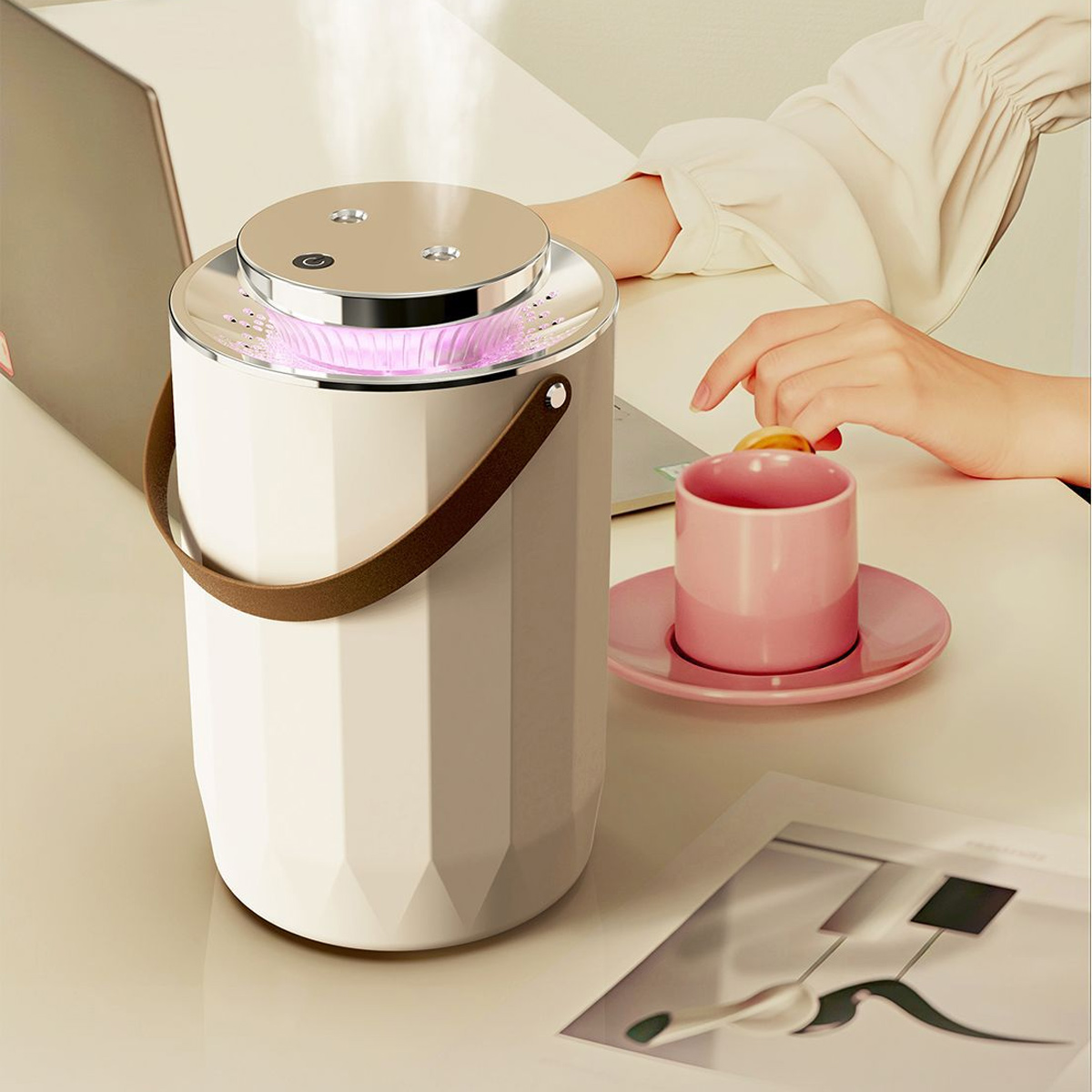 Ein weißer Luftbefeuchter mit braunem Griff steht auf einem Schreibtisch. Eine rosa Tasse und Untertasse befinden sich in der Nähe, ebenso wie eine Hand, die nach einer Zitrone greift.