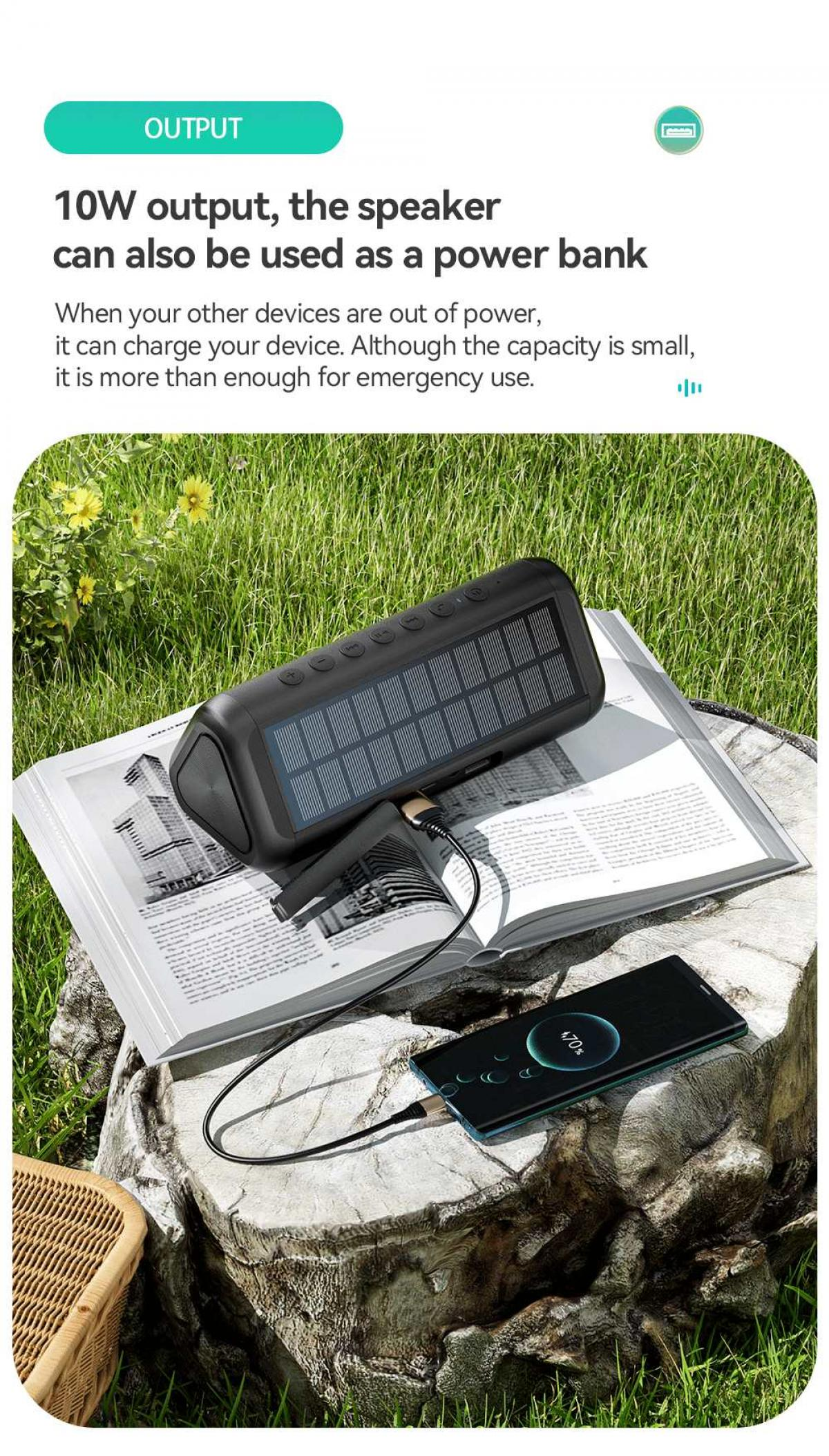 Ein schwarzer Lautsprecher mit Solarpanelen lädt ein Telefon. Es liegt auf einem Buch auf einem Baumstumpf, mit Gras im Hintergrund.