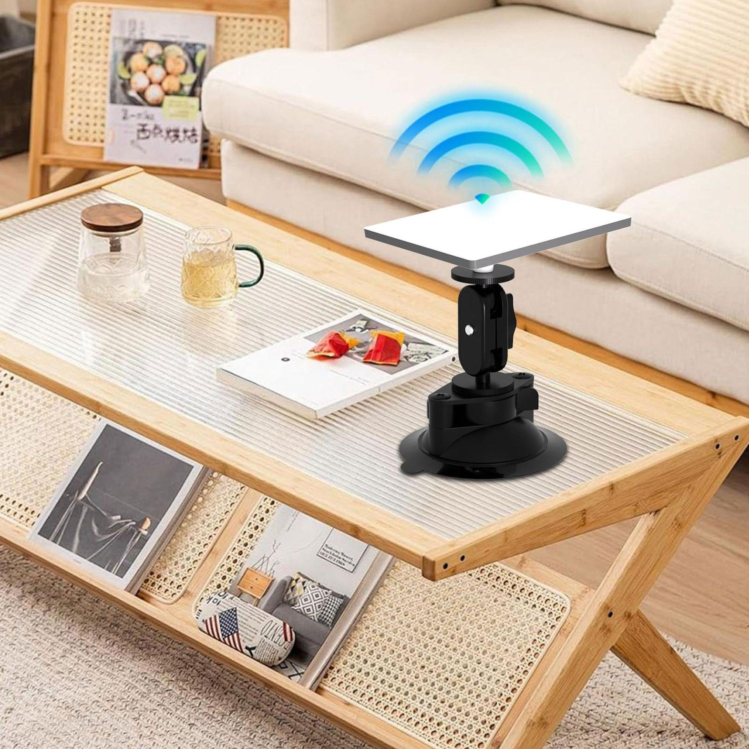 Un tavolino con un dispositivo che emette segnali wifi. C'è un bicchiere, una tazza e delle riviste. Un divano è sullo sfondo.