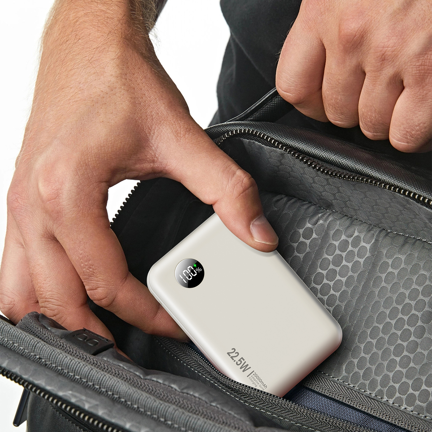 Una persona mette un power bank bianco in una borsa grigia. Il power bank mostra il 100% di carica.