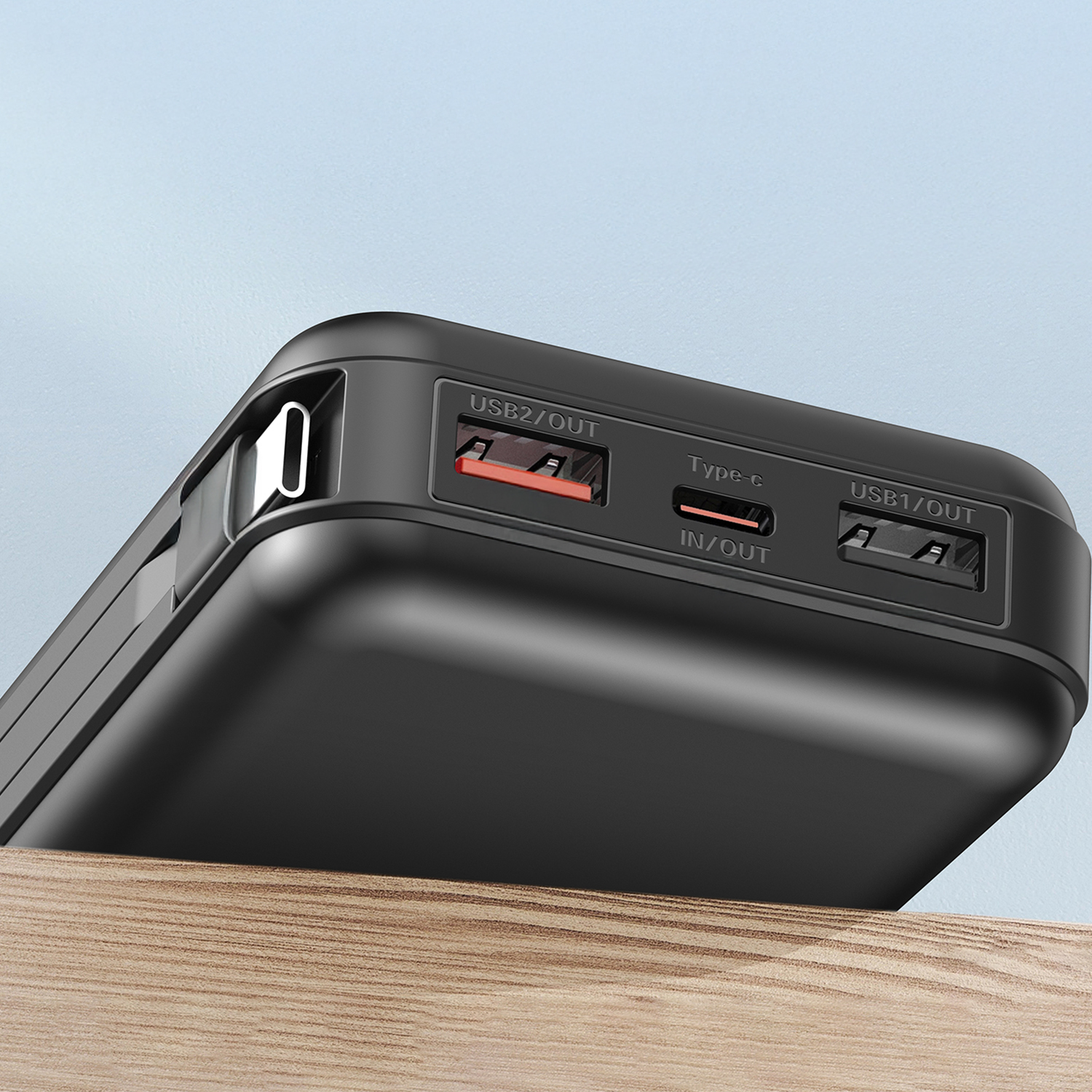 Primo piano di un power bank nero con porte USB, su una superficie di legno, contro uno sfondo azzurro chiaro.