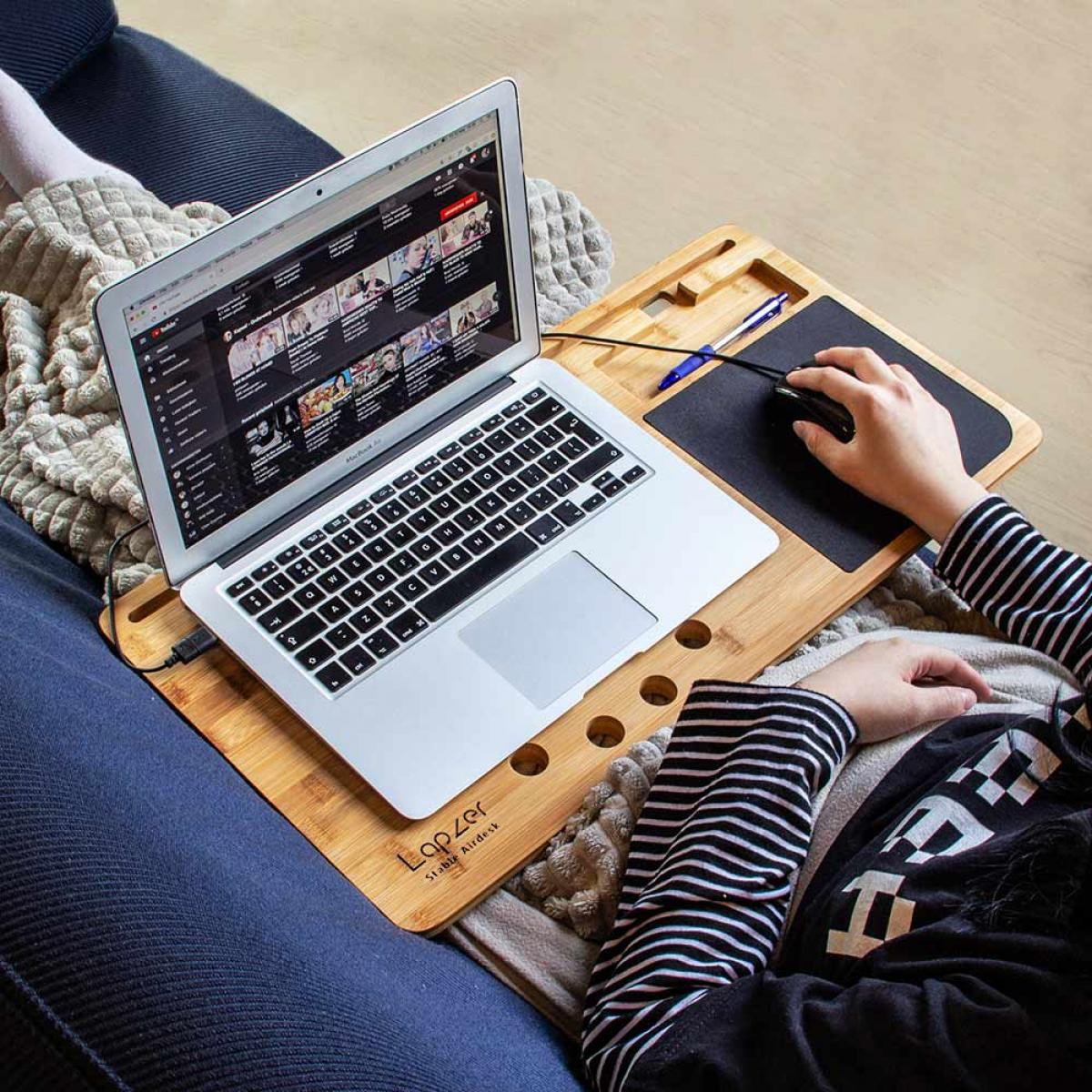 Person using a laptop on a wooden desk. YouTube is open. Hand holding mouse. The person is wearing a striped shirt.