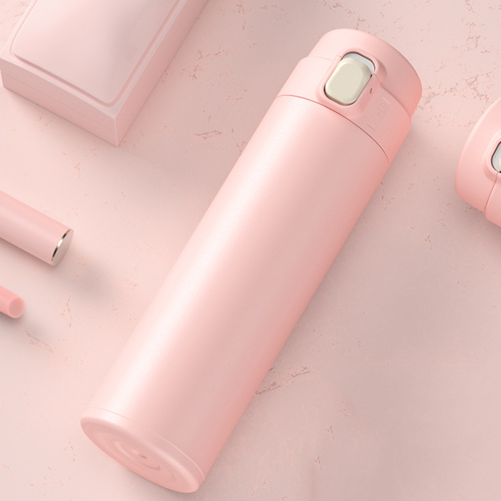 Eine rosa Thermosflasche mit einem weißen Knopf auf einer rosa Oberfläche. Im Hintergrund befinden sich weitere rosa Objekte. Die Szene ist weich und gut beleuchtet.