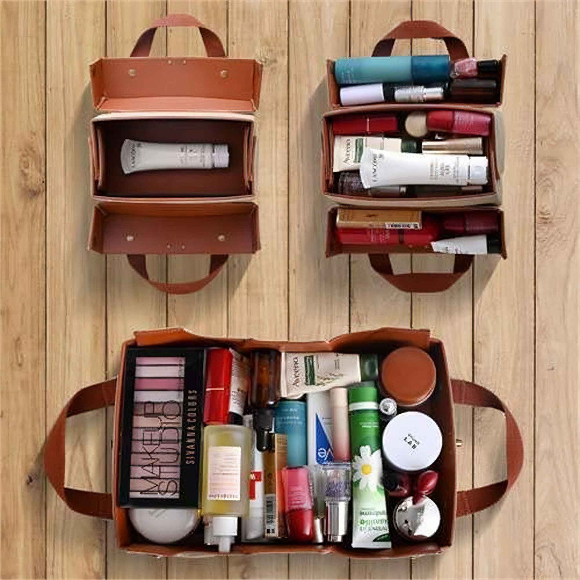 Drei offene braune Make-up-Taschen mit verschiedenen Kosmetika auf Holzgrund. Jede Tasche hat einen Griff.