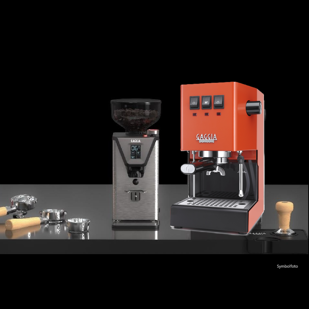 Eine orangefarbene Gaggia Classic Espressomaschine und eine silberne Kaffeemühle mit Zubehör auf schwarzer Oberfläche.
