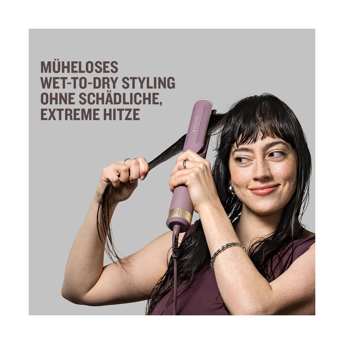 Una donna usa uno strumento per lo styling dei capelli viola. Tiene una ciocca di capelli bagnati, sorridendo. Testo tedesco sullo sfondo.