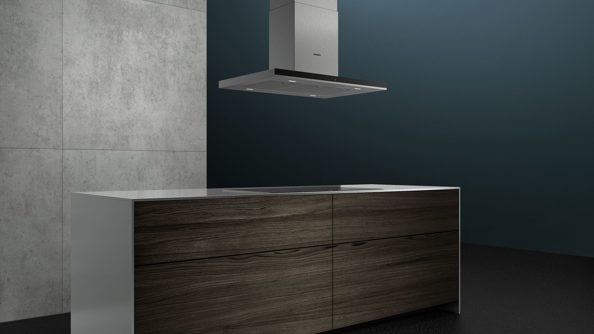 Interni della cucina. Armadi in legno con piano di lavoro bianco. Cappa aspirante in acciaio inox. Parete in cemento grigio sullo sfondo.