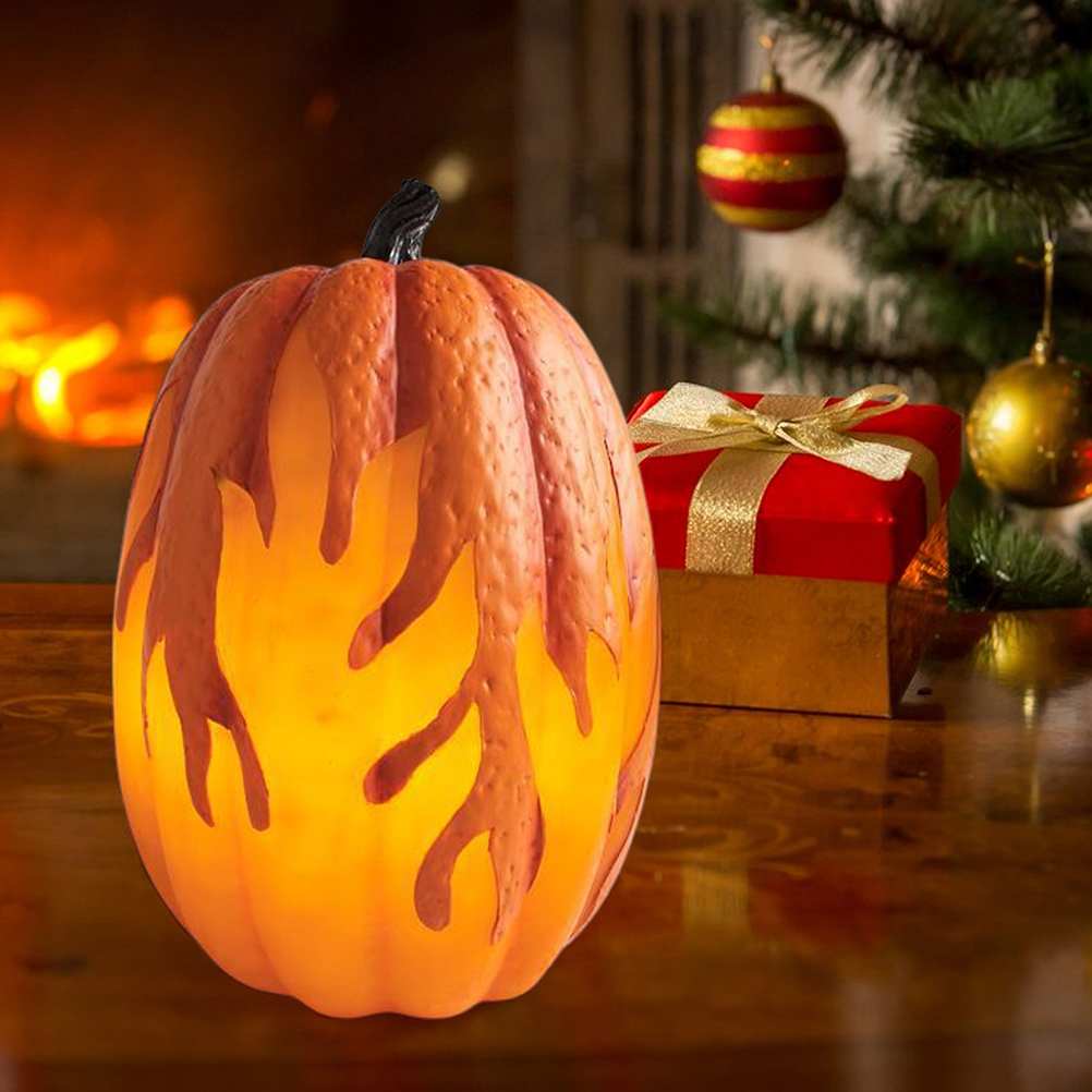 Ein orangefarbener, beleuchteter Kürbis mit Flammenausschnitten, eine rote Geschenkbox mit goldener Schleife und ein geschmückter Weihnachtsbaum.