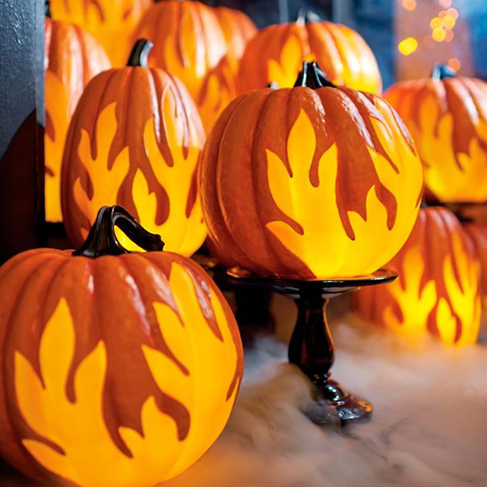 Orange Kürbisse mit flammförmigen Ausschnitten sind von innen beleuchtet. Einige stehen auf einem Tisch mit Nebel.