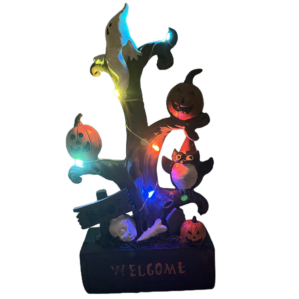 Halloween-Dekoration mit Kürbissen, Geist, Katze und Schädel auf einem Baumstammfuß. Lichter schreiben 'Willkommen'.