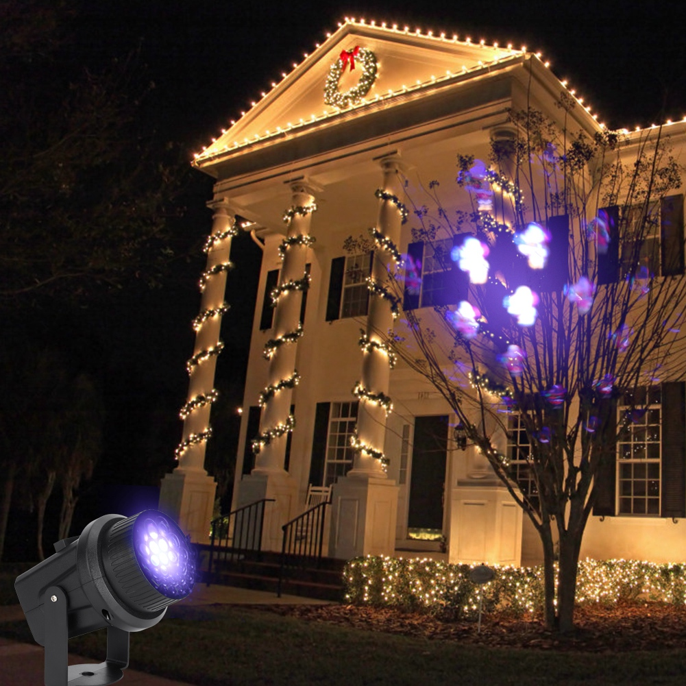 Ein Haus bei Nacht ist mit Weihnachtsbeleuchtung geschmückt. Ein Projektor strahlt lila Lichter aus. Ein Kranz hängt über der Tür.