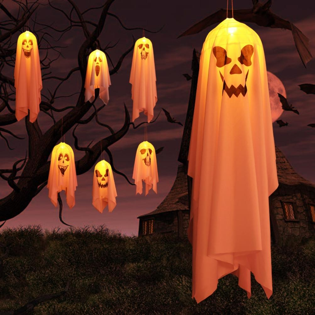 Halloweenszene mit hängenden Geisterdekorationen mit geschnitzten Gesichtern. Dunkle Äste, Fledermäuse, Vollmond und ein Haus im Hintergrund.