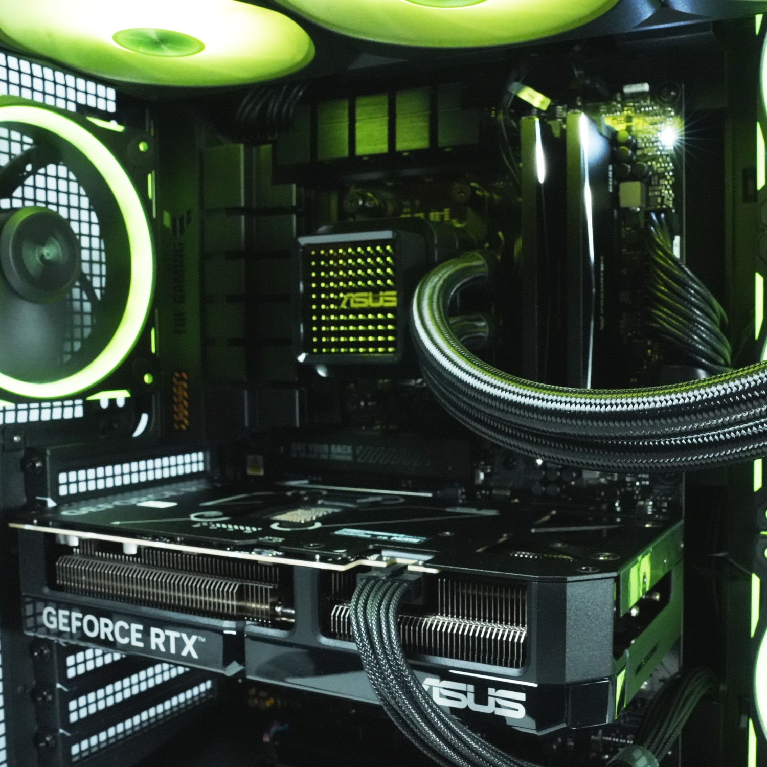 Dentro de una caja de ordenador, se ve una tarjeta gráfica con 'GEFORCE RTX'. Ventiladores y componentes iluminados en verde. Logo ASUS.