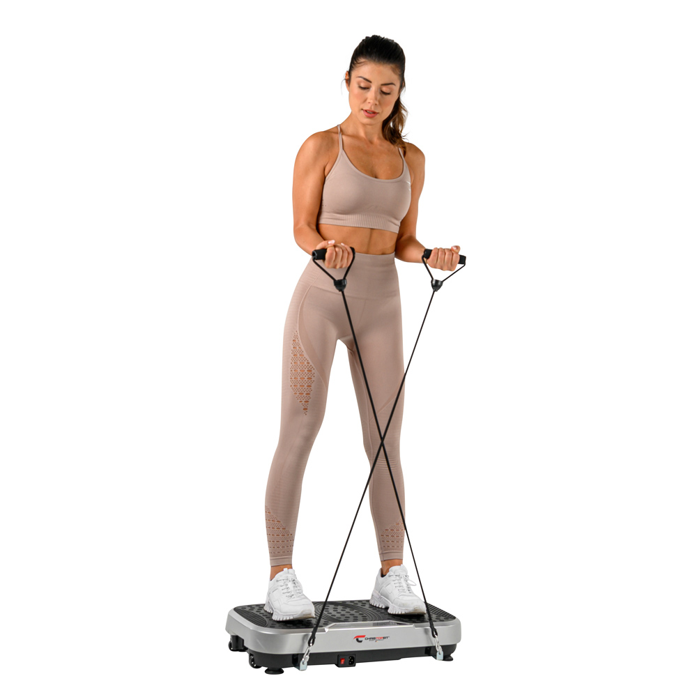 Eine Frau trainiert auf einer Vibrationsplatte. Sie trägt beige Sportkleidung und hält Widerstandsbänder. Weißer Hintergrund.