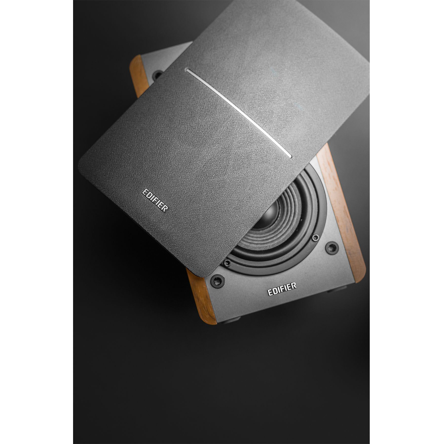 Dwa głośniki Edifier na czarnej powierzchni. Jeden ma otwartą pokrywę, odsłaniającą głośnik. Drugi jest częściowo widoczny.