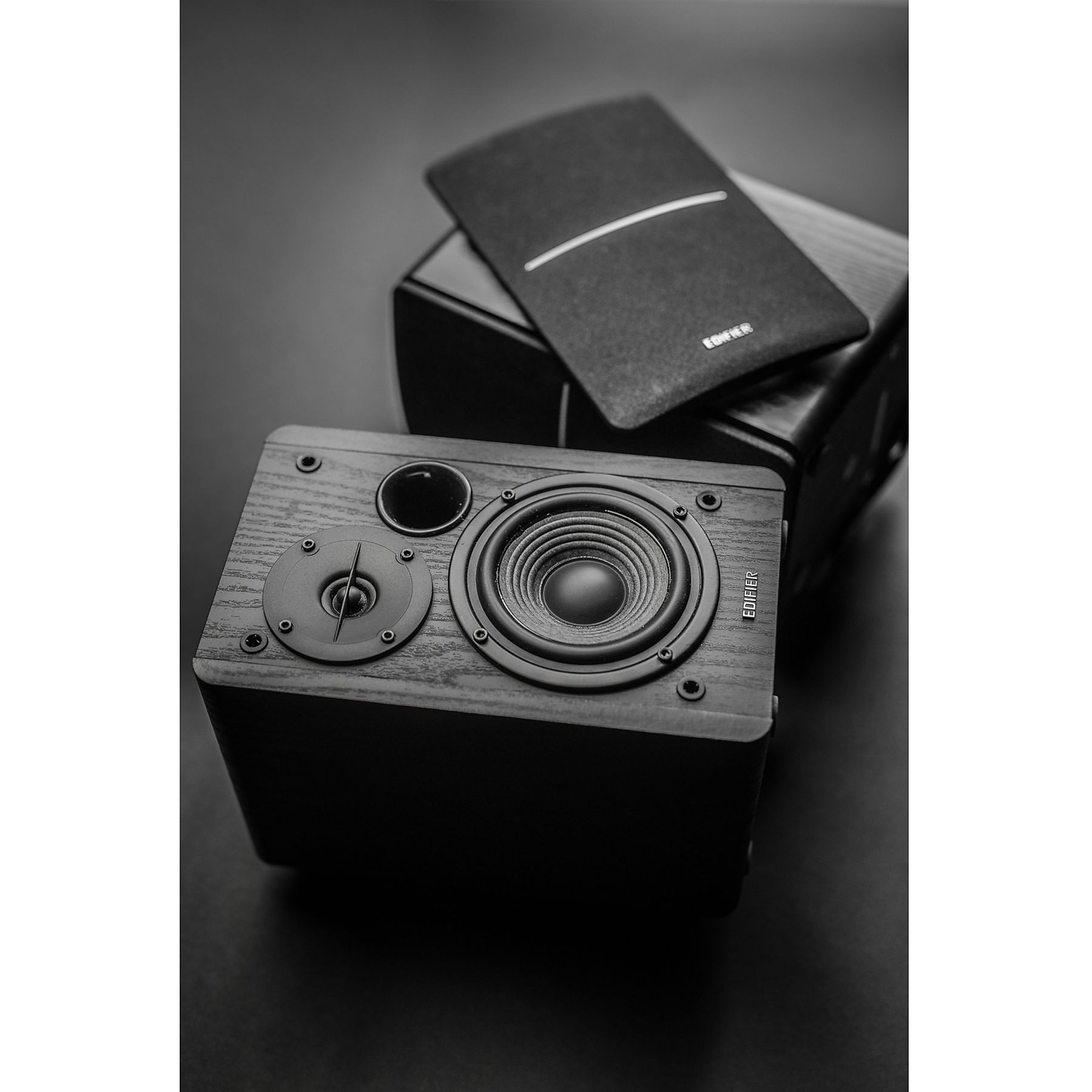 Czarne głośniki z osłoną na ciemnej powierzchni. Widoczne membrany głośników, marka Edifier.