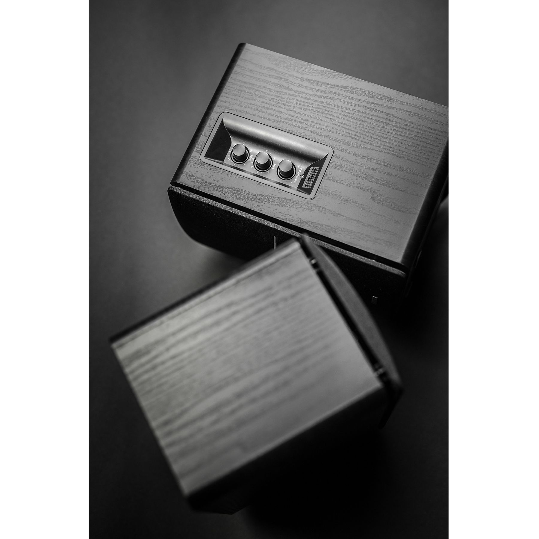 Dwa czarne głośniki na czarnym tle. Jeden jest skierowany w stronę drugiego. Widoczne elementy sterujące.