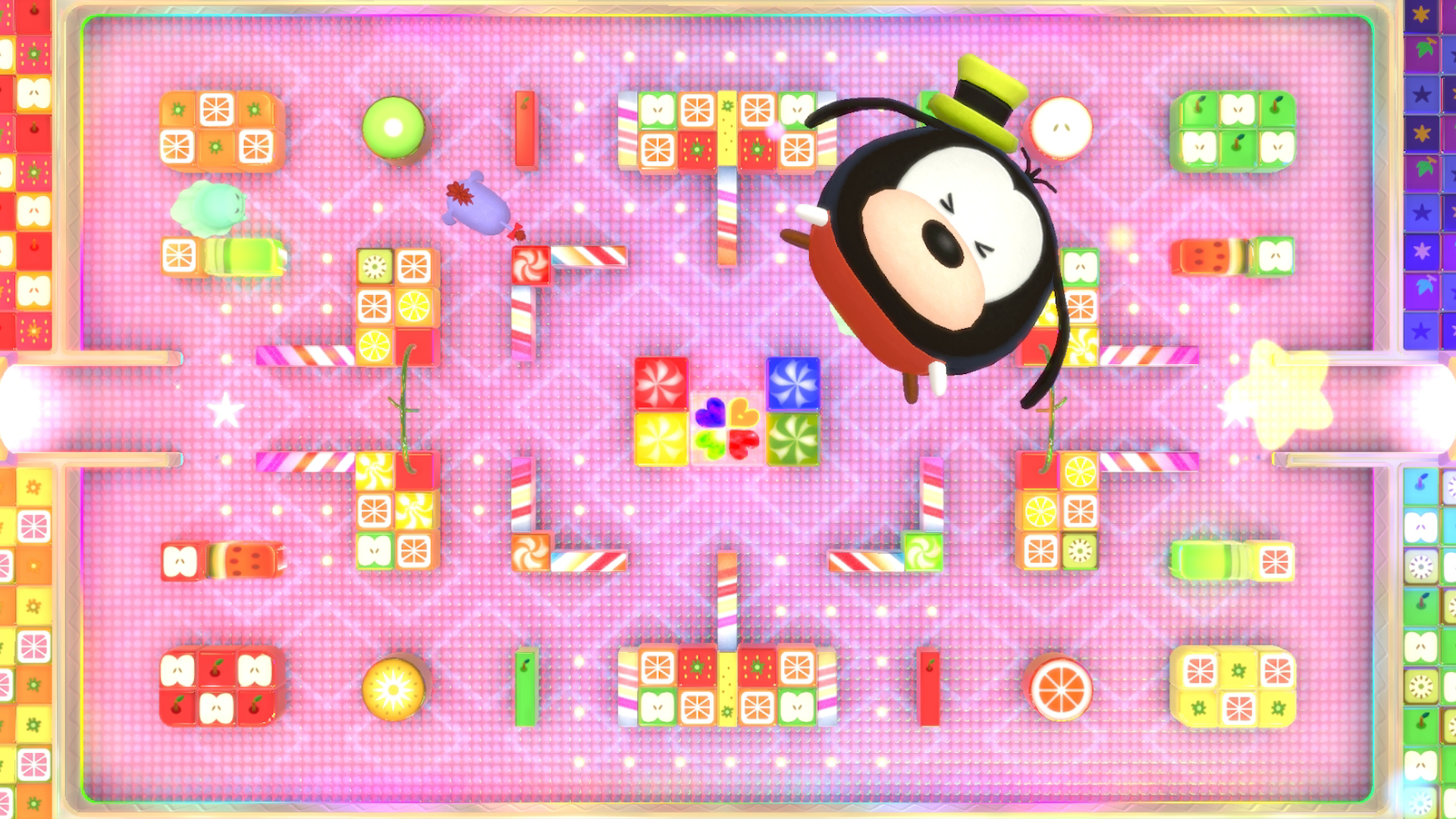 Kreskówkowa postać w kapeluszu unosi się nad kolorową planszą pełną cukierków i owoców.