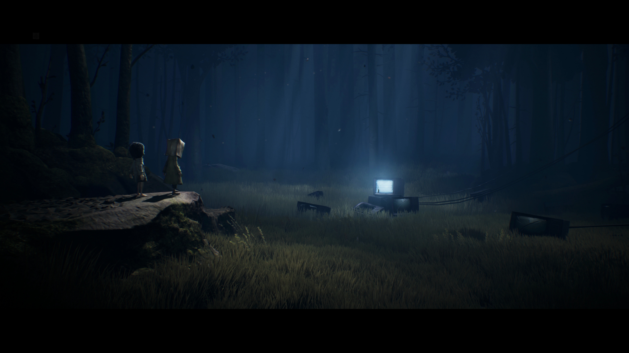 Dos figuras están de pie sobre una roca en un bosque oscuro. Un televisor brillante está en la hierba. La escena es oscura y misteriosa.