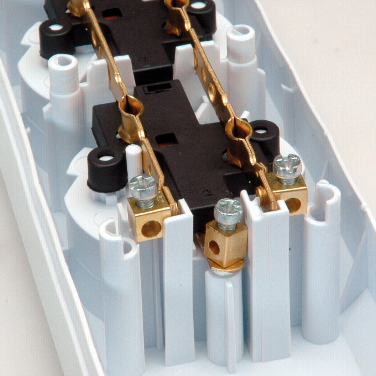 Zbliżenie elementów elektrycznych w białej plastikowej obudowie. Widoczne mosiężne złącza, śruby i czarne elementy z tworzywa sztucznego.