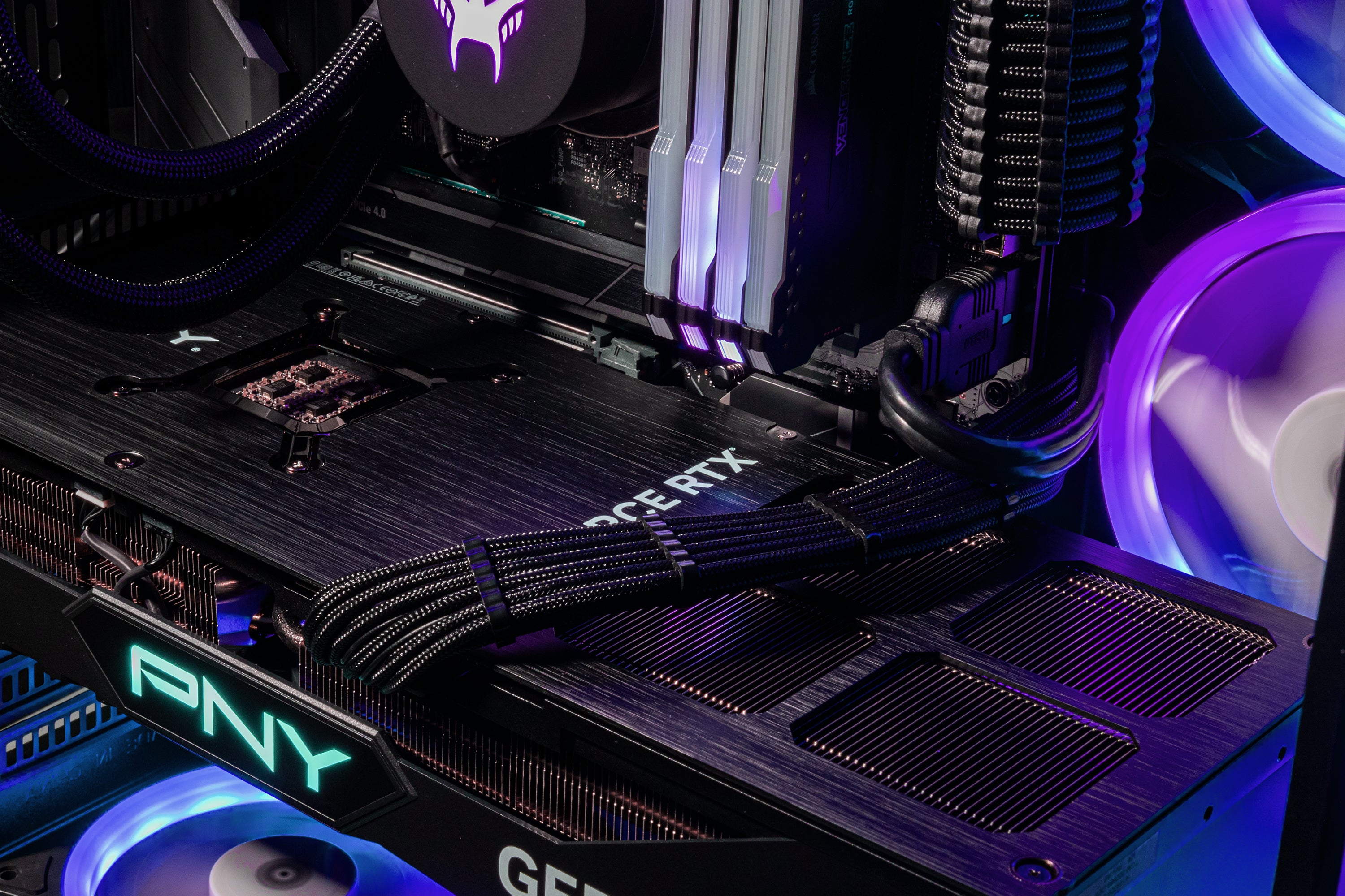Nahaufnahme eines Gaming-PC-Innenraums. GPU, RAM, Lüfter und Kabel sind sichtbar. Lila und blaue Beleuchtung hebt die Komponenten hervor.