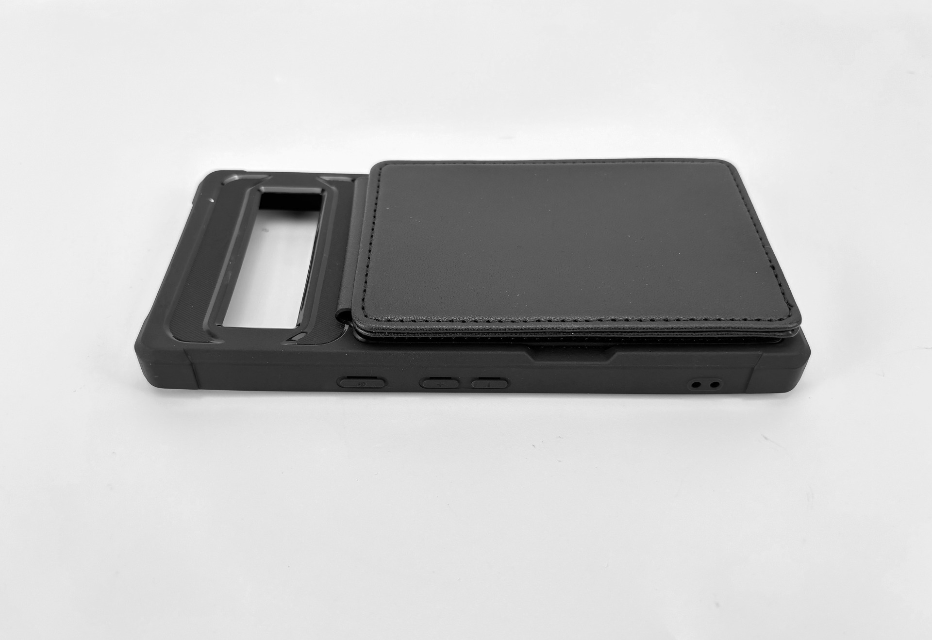 Eine schwarze Handyhülle mit Klappdeckel liegt auf einer weißen Oberfläche. Die Hülle hat eine rechteckige Öffnung für die Kamera.