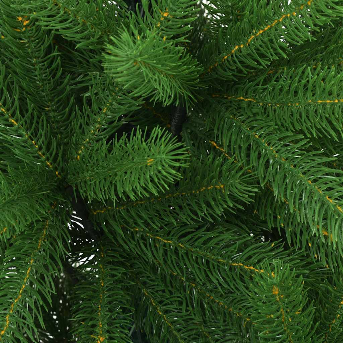 Nahaufnahme eines grünen künstlichen Weihnachtsbaumes. Die Nadeln sind dicht und detailliert, mit gelben Akzenten. Dunkler Stamm sichtbar.