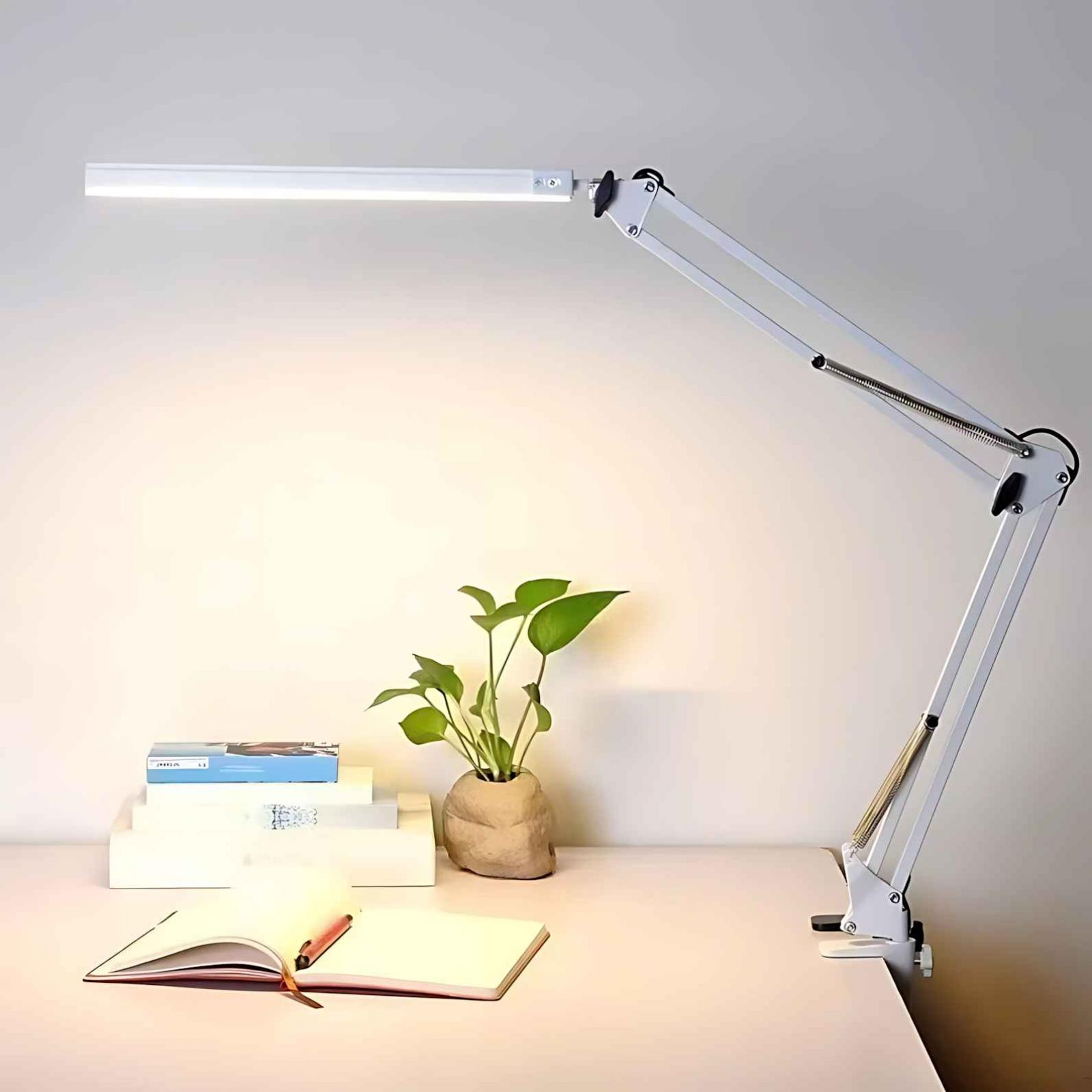 Eine weiße Schreibtischlampe befindet sich über einem Schreibtisch. Eine Pflanze und Bücher stehen auf dem Schreibtisch.