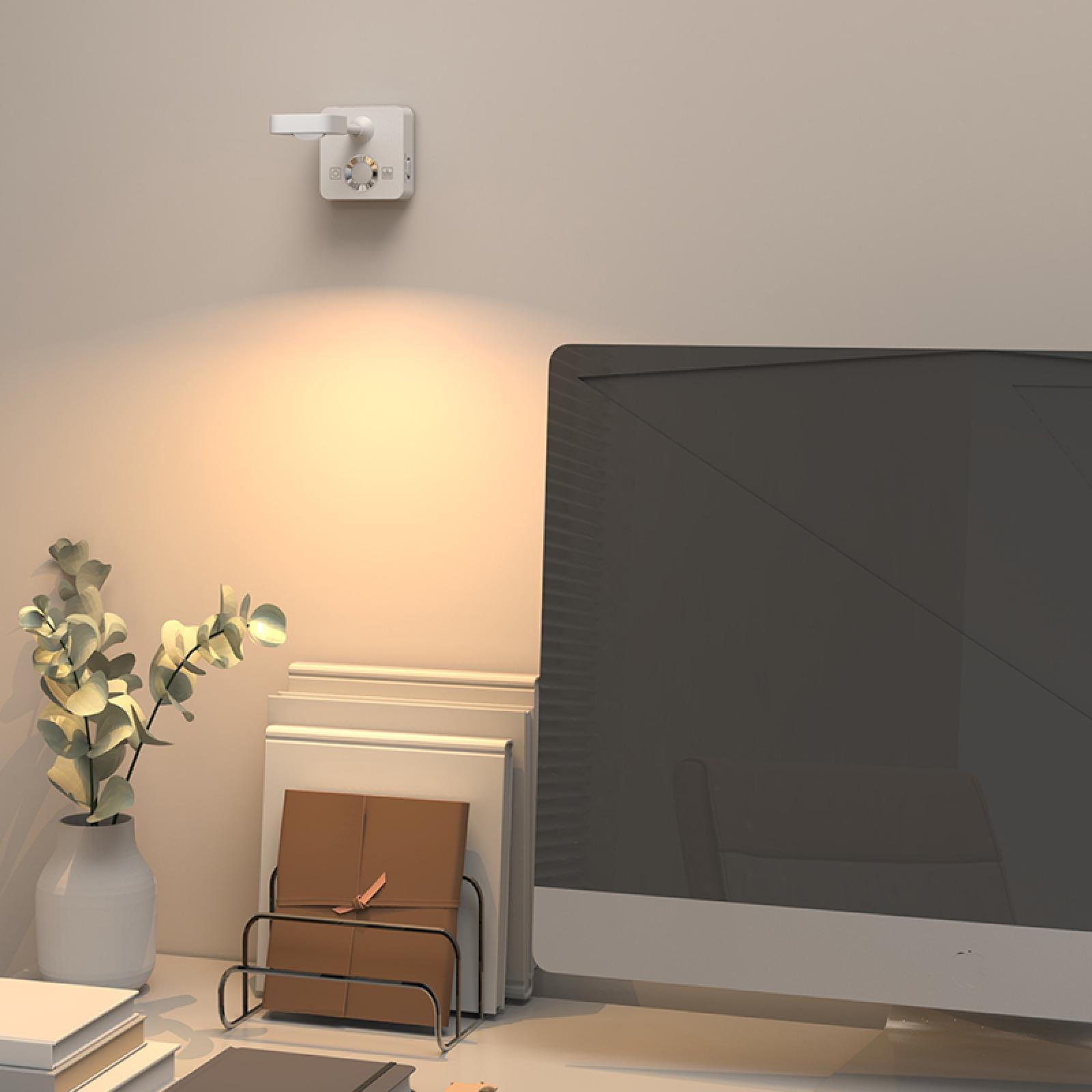 Ein Schreibtisch mit Computer, Lampe, Pflanze in einer Vase und Büchern. Warmes Licht ist vorhanden.