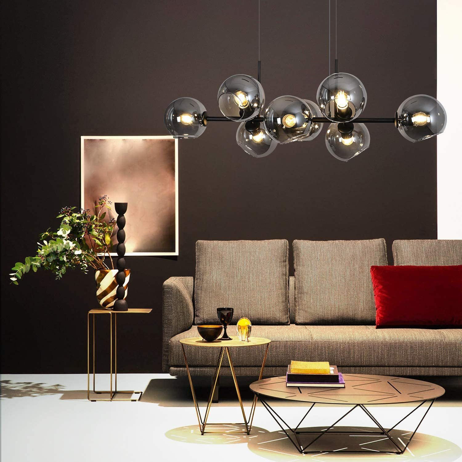 Wohnzimmerszene mit Sofa, Couchtischen und modernem Kronleuchter. Ein rotes Kissen liegt auf dem Sofa. Blumen und Dekoration sind ebenfalls vorhanden.