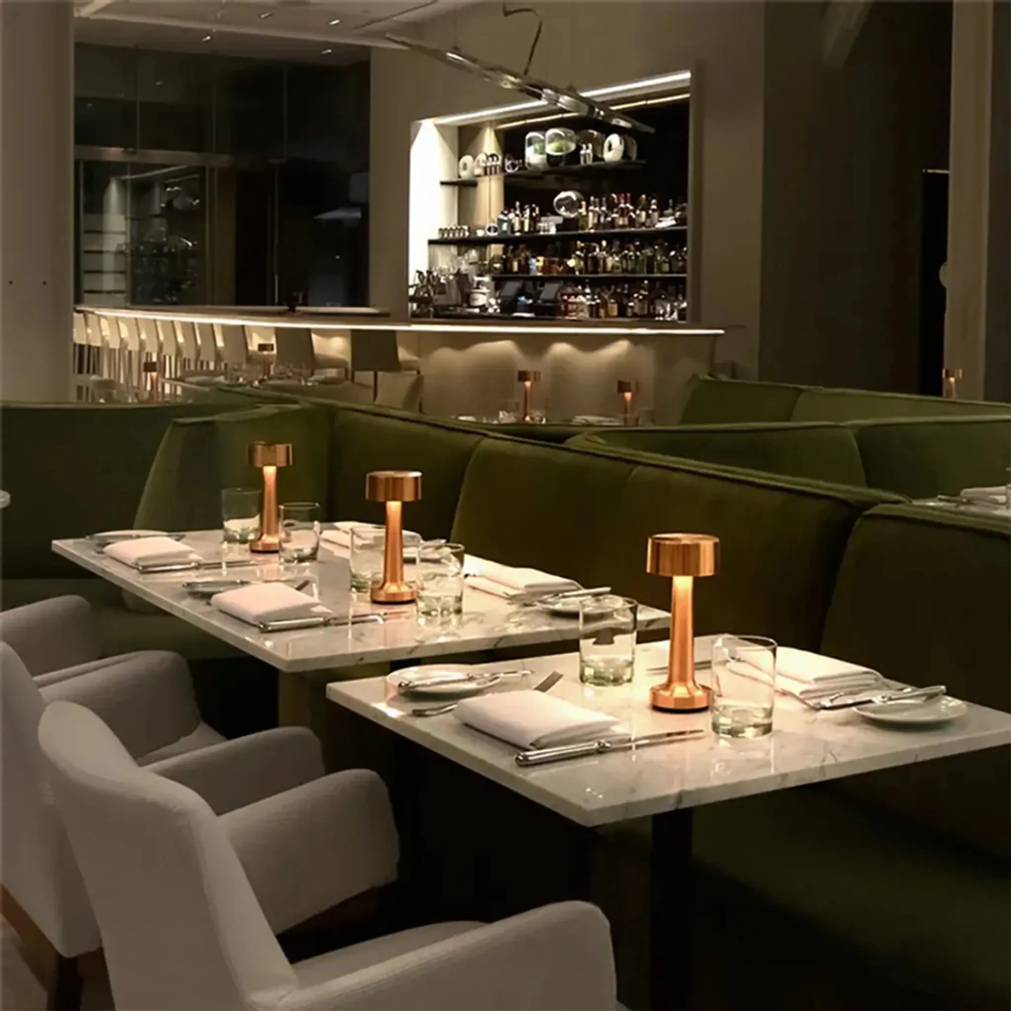 Restaurantinterieur mit gedeckten Tischen. Grüne Sitzecken, weiße Stühle und eine Bar im Hintergrund. Kupferlampen auf Tischen.